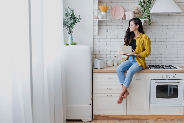 Mulher de tiro completo com livro na cozinha