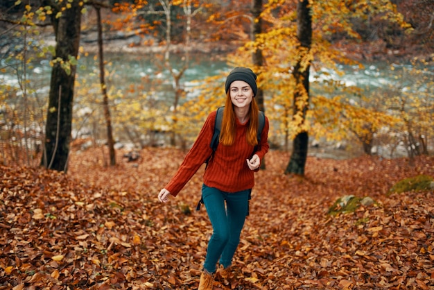 Mulher de turismo de viagens de suéter e jeans na floresta de outono perto do rio da montanha