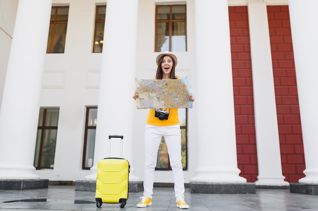 Mulher de turista viajante chocado em roupas casuais com câmera de foto vintage retrô mala segurar mapa da cidade na cidade ao ar livre. Garota viajando para o exterior para viajar no fim de semana. Estilo de vida da viagem de turismo.