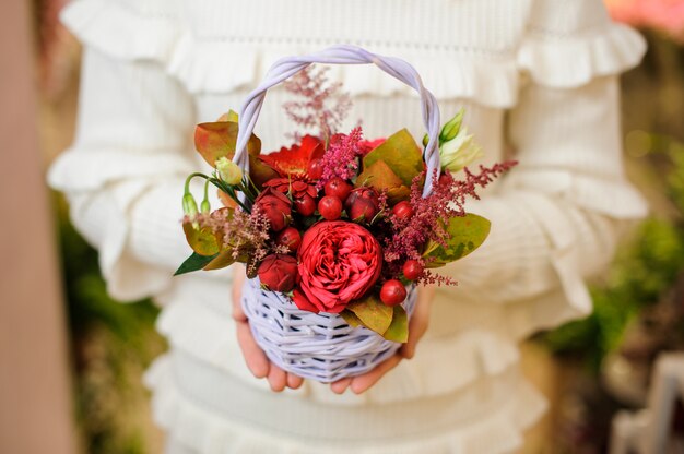 Mulher de um suéter branco segurando uma cesta de vime fofa com composição de flores dos namorados