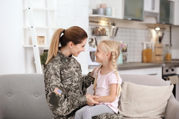 Mulher de uniforme militar com sua filha no sofá em casa