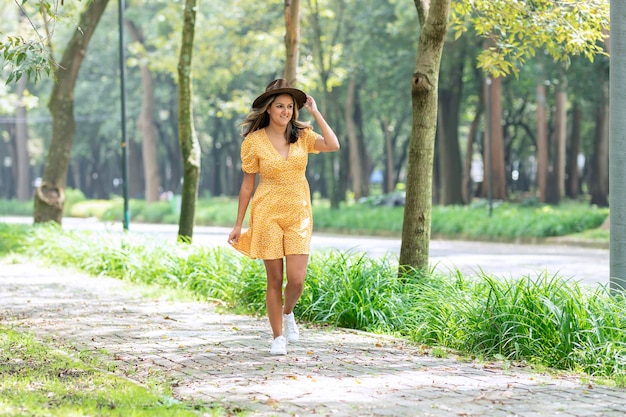 Mulher de vestido amarelo caminha pela calçada em um parque