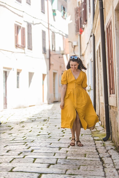 Mulher de vestido amarelo com chapéu de palha andando pela antiga cidade turística na croácia