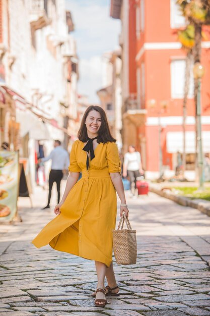 Mulher de vestido amarelo com chapéu de palha, caminhando pela antiga cidade turística de Porec, na Croácia