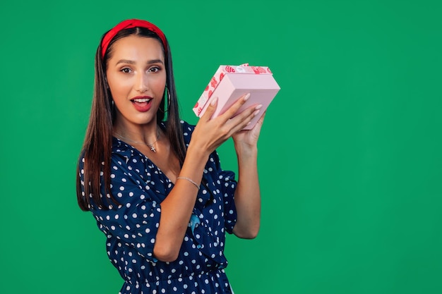 Mulher de vestido azul segurando uma caixa de presente perto de sua orelha e liste