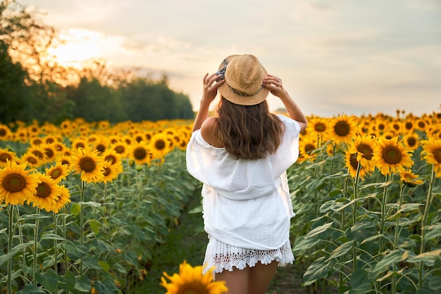 Mulher de vestido branco e chapéu de palha posando no campo de girassol