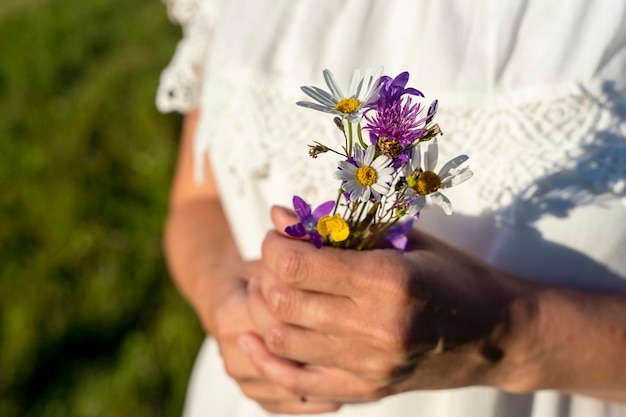 Mulher de vestido branco tem um buquê de flores silvestres nas mãos