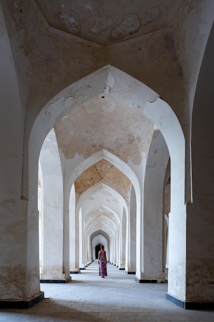 Mulher de vestido colorido fica em longa colunata coberta com telhado em arco Bukhara Uzbequistão