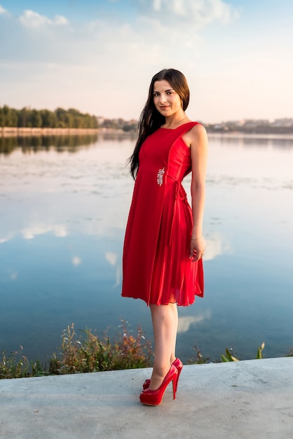 Mulher de vestido comprido em pé na praia ao pôr do sol