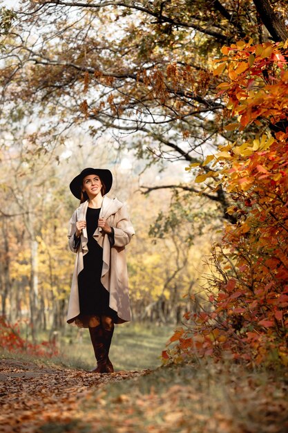 Mulher de vestido e chapéu no fundo da folhagem de outono