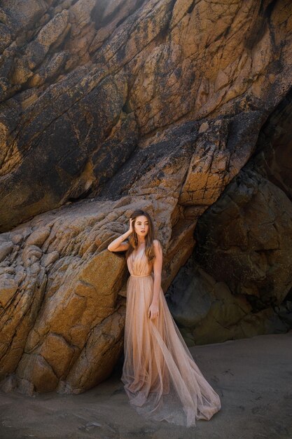 Mulher de vestido longo perto de rochas e oceano