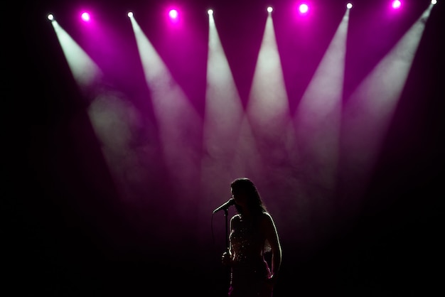 Mulher de vestido longo, realizando no palco. mulher cantando no palco em frente às luzes.