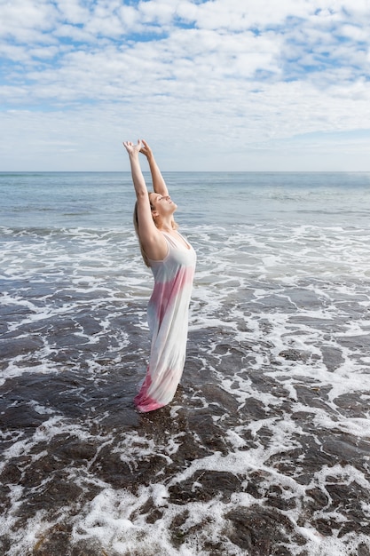 Mulher de vestido no mar curtindo sua liberdade com os braços para cima