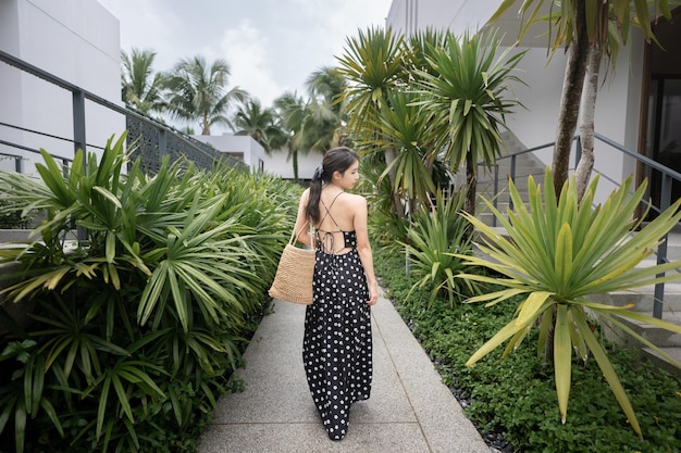 Mulher de vestido preto com cesta de palha andando no hotel resort tropical