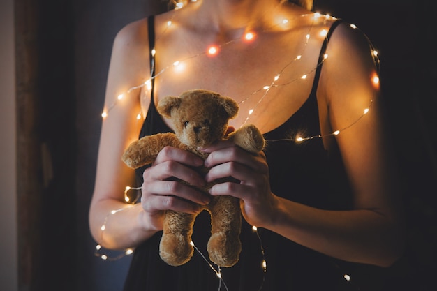 Mulher de vestido preto e luzes segurando o ursinho de pelúcia brinquedo