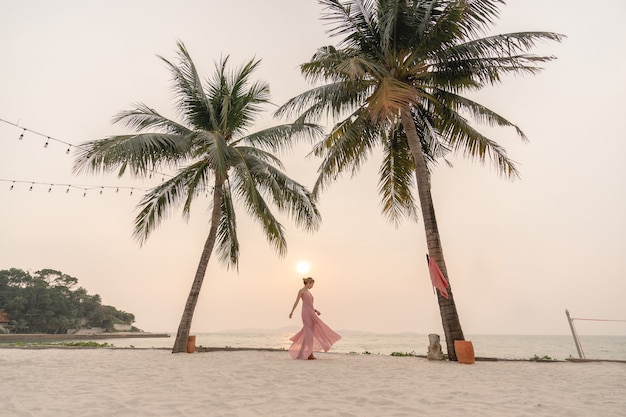 Mulher de vestido rosa curtindo o lindo pôr do sol na praia