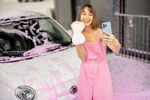 Mulher de vestido rosa tira selfie no telefone enquanto lava o carro