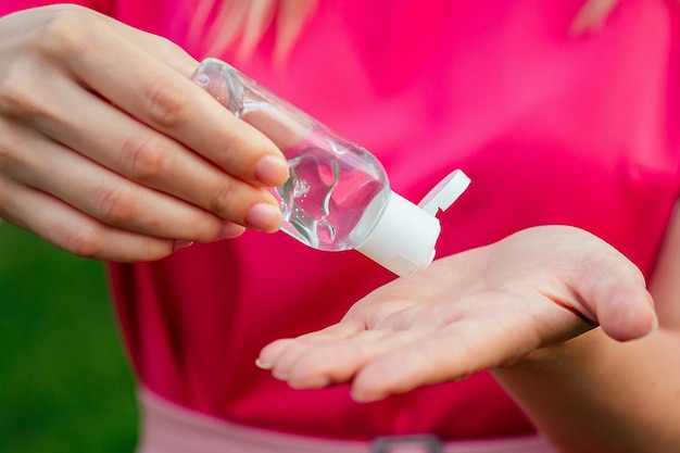 Mulher de vestido rosa usando gel antisséptico antibacteriano no parque de verão