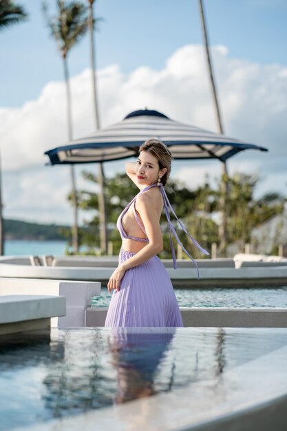 Mulher de vestido roxo posando à beira da piscina com vista para o mar