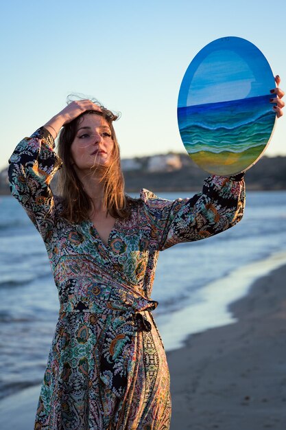 Foto mulher de vestido segurando um quadro pintado