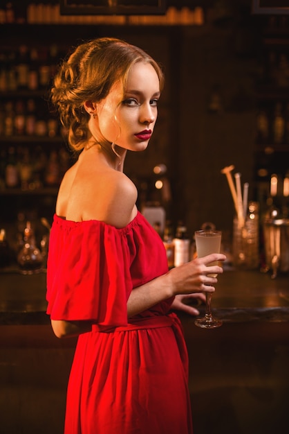 Mulher de vestido vermelho em pé no balcão do bar