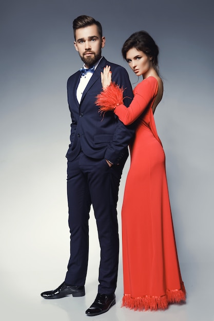 Mulher de vestido vermelho lindo e homem vestindo terno clássico azul com gravata borboleta.