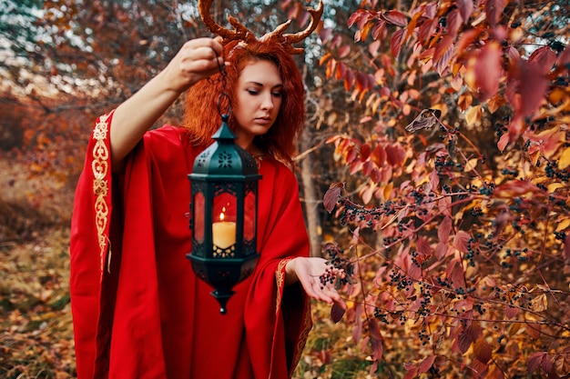 Mulher de vestido vermelho longo com chifres de veado na floresta de outono.