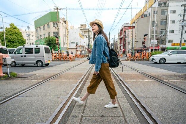 mulher de viagem relaxada atravessando a ferrovia segurando seu telefone na cidade de osaka, no japão.