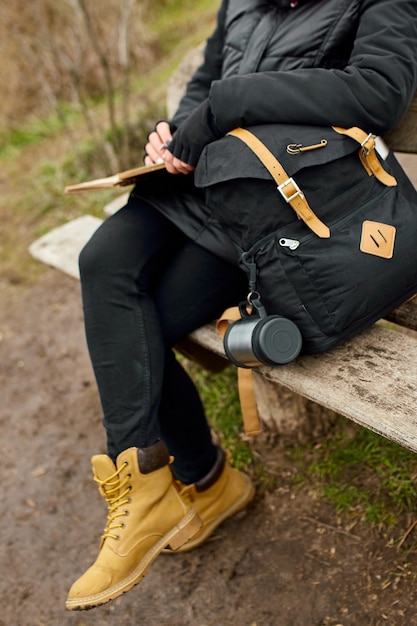 Mulher de viagens com chapéu vermelho em jaqueta preta escrever no caderno, fazer anotações, desenhar um esboço contra a vista do rio, viagens locais, saúde mental. Outono