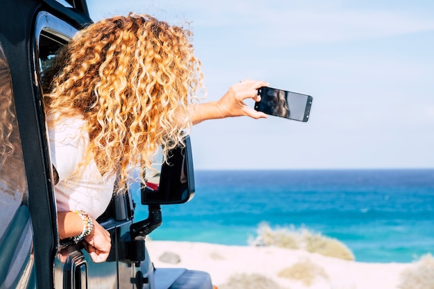 Mulher de viagens feliz e aproveite o destino de praia e mar tirando fotos do telefone inteligente de dentro de seu carro - mulheres livres dirigem e se divertem nas férias de verão - oceano ao ar livre