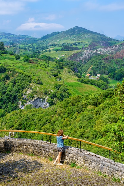 Mulher debruçada sobre um miradouro contemplando a paisagem verde do vale