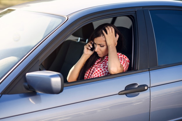 Mulher decepcionada na camisa vermelha, dirigindo o carro caro, falando no smartphone enquanto dirige.