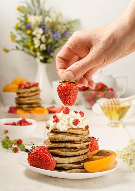 Mulher decora morangos com uma pilha de panquecas com creme chantilly