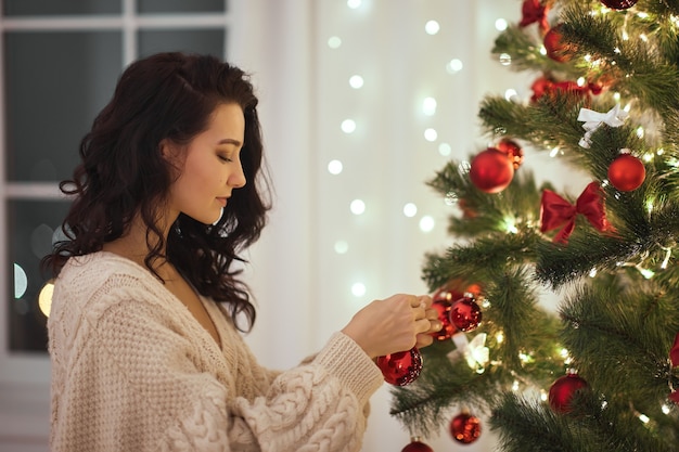 Mulher decorando árvore de natal com brinquedos de árvore de natal em casa