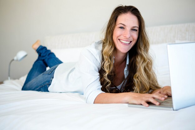 Mulher deitada em sua cama em seu laptop, sorrindo