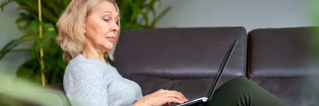 Mulher deitada em um sofá em casa, concentrando-se enquanto ela trabalha em um laptop.