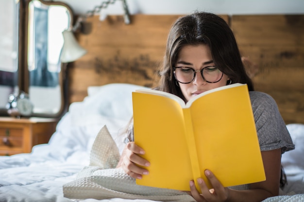 Mulher deitada na cama e lendo o livro