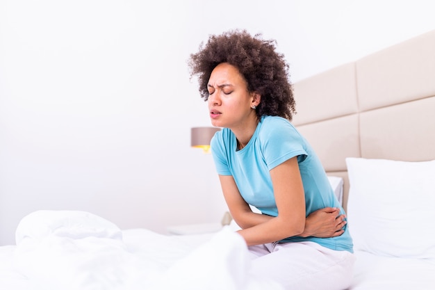 Mulher deitada na cama, olhando doente na sala de estar. jovem deitada na cama e de mãos dadas na barriga.