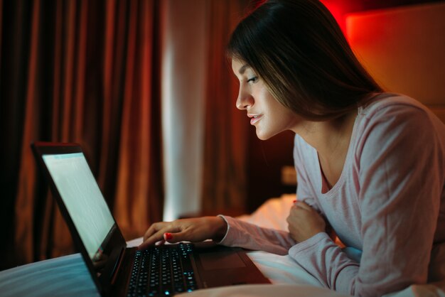 Mulher deitada na cama olhando para a tela do laptop