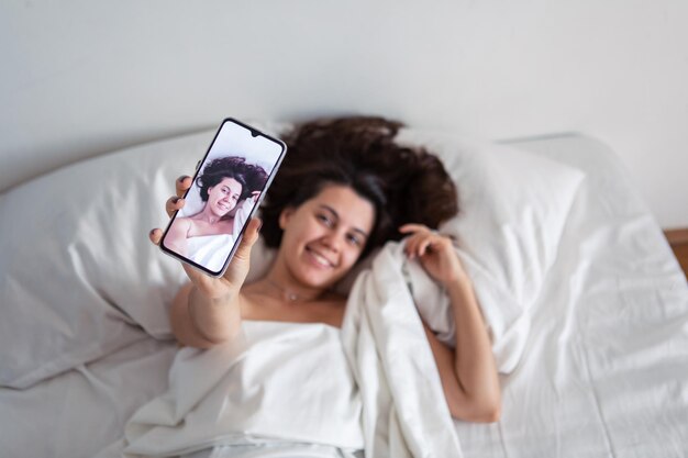 Mulher deitada na cama tomando selfie no telefone