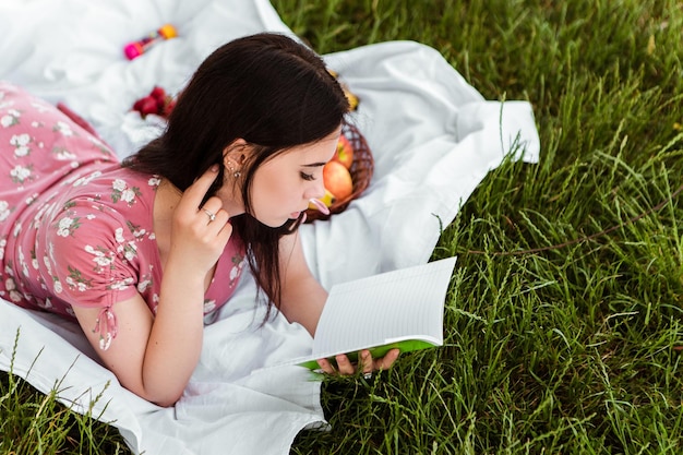 Mulher deitada no lençol branco, lendo livro, sorrindo