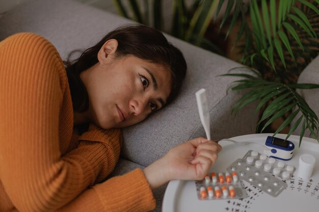 Foto mulher deitada no sofá doente e com medicamentos à mão