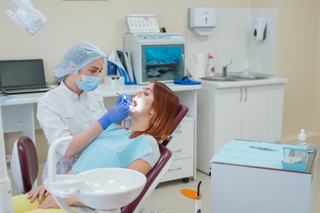 Mulher dentista checando seu paciente em busca de cárie Mulher ruiva examinada por um médico A menina fará a saúde dos dentes