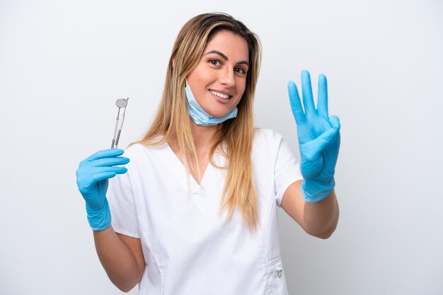 Mulher dentista segurando ferramentas isoladas em fundo branco feliz e contando três com os dedos