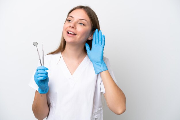 Mulher dentista segurando ferramentas isoladas em fundo branco ouvindo algo colocando a mão na orelha