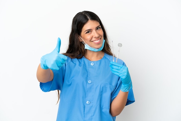 Mulher dentista segurando ferramentas sobre um fundo branco isolado com o polegar para cima porque algo bom aconteceu