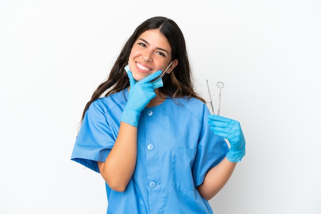 Mulher dentista segurando ferramentas sobre um fundo branco isolado, feliz e sorridente