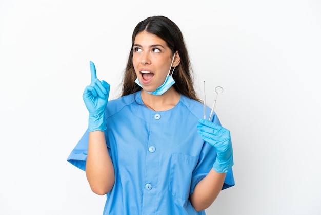 Mulher dentista segurando ferramentas sobre um fundo branco isolado, pensando em uma ideia apontando o dedo para cima