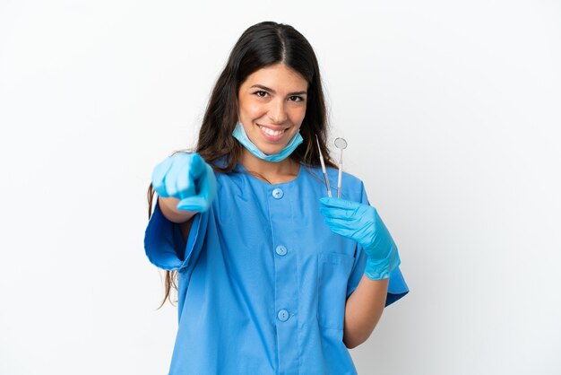 Mulher dentista segurando ferramentas sobre um fundo branco isolado surpresa e apontando para a frente