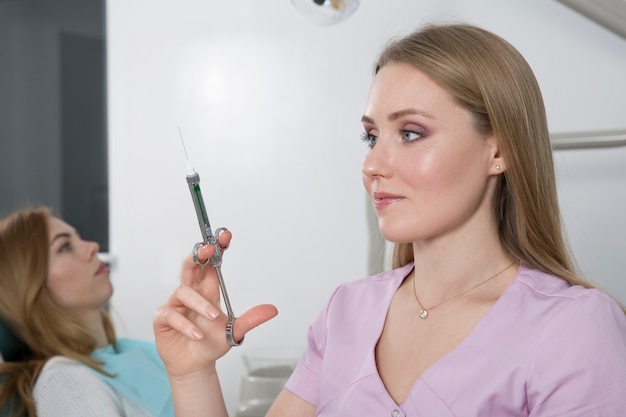 Mulher dentista segurando uma seringa no contexto de um consultório dentista